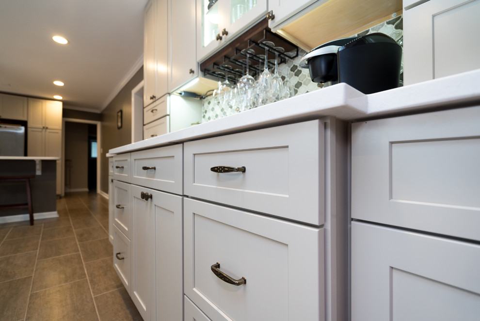 Transitional l-shaped laminate floor home design photo in DC Metro with a farmhouse sink, shaker cabinets, white cabinets, quartz countertops, gray backsplash, porcelain backsplash, stainless steel appliances and a peninsula