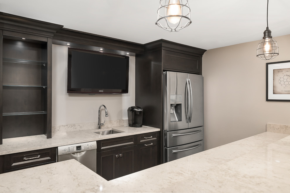 Large transitional l-shaped wet bar in Chicago with an undermount sink, shaker cabinets, black cabinets, quartz benchtops, vinyl floors, brown floor and beige benchtop.
