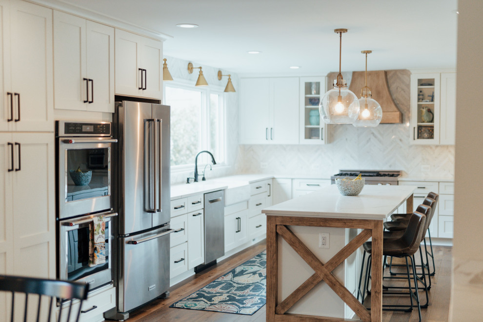 Foto på ett stort lantligt vit linjärt kök och matrum, med en rustik diskho, luckor med profilerade fronter, vita skåp, marmorbänkskiva, vitt stänkskydd, stänkskydd i keramik, svarta vitvaror, en köksö och brunt golv