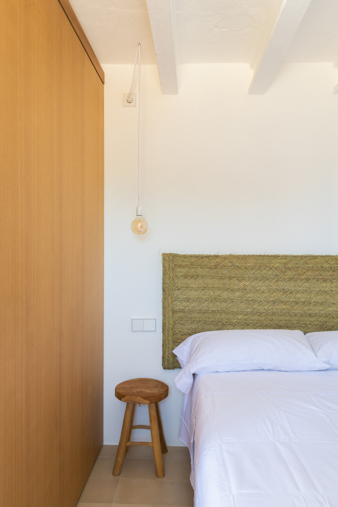 Ejemplo de habitación de invitados beige y blanca mediterránea pequeña con paredes blancas, suelo beige y vigas vistas