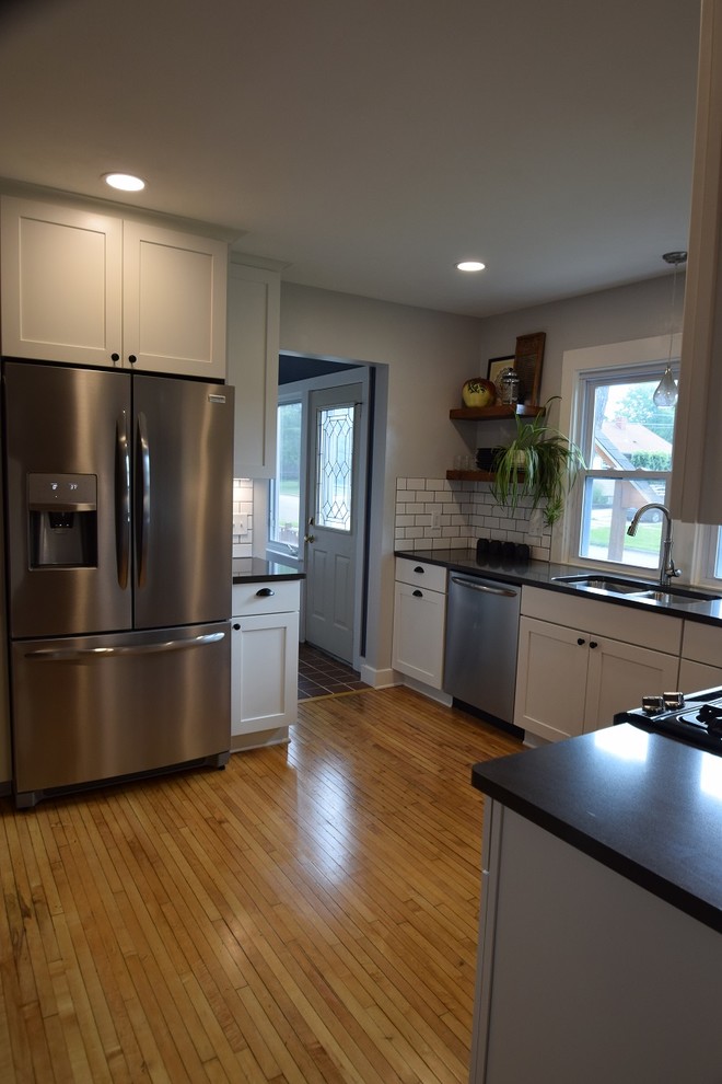 Kitchen - transitional u-shaped light wood floor kitchen idea with an undermount sink, shaker cabinets, white cabinets, quartz countertops, white backsplash, subway tile backsplash, stainless steel appliances, no island and black countertops