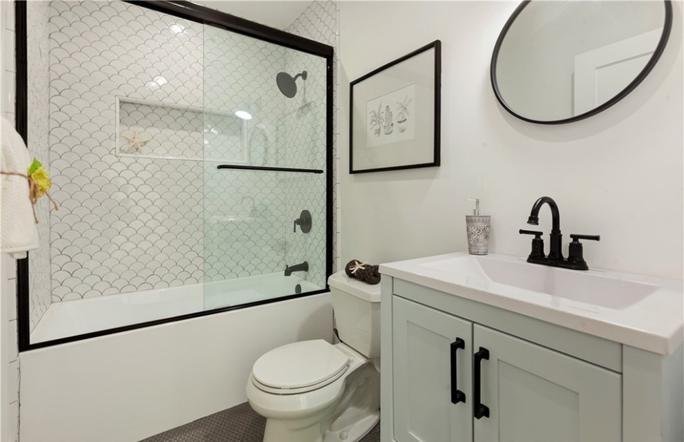 На фото: ванная комната в классическом стиле с фасадами в стиле шейкер, серыми фасадами, ванной в нише, душем над ванной, белой плиткой, керамической плиткой, белыми стенами, полом из керамической плитки, монолитной раковиной, столешницей из нержавеющей стали, черным полом, душем с раздвижными дверями, белой столешницей, нишей, тумбой под одну раковину и напольной тумбой