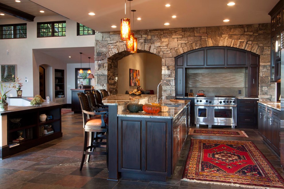 Huge transitional l-shaped slate floor kitchen photo with a single-bowl sink, beaded inset cabinets, dark wood cabinets, granite countertops, green backsplash, cement tile backsplash, stainless steel appliances, brown walls and an island
