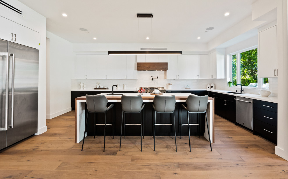 This is an example of a large contemporary l-shaped open plan kitchen in Los Angeles with an undermount sink, marble benchtops, white splashback, stainless steel appliances, with island and multi-coloured benchtop.