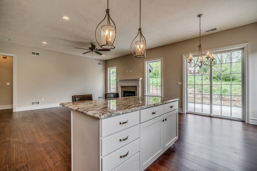 Transitional l-shaped bamboo floor and brown floor eat-in kitchen photo with an undermount sink, flat-panel cabinets, white cabinets, granite countertops, brown backsplash, subway tile backsplash, stainless steel appliances, an island and brown countertops