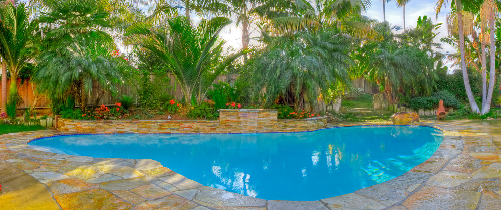 Photo of a large tropical backyard kidney-shaped lap pool in San Diego with a water feature and natural stone pavers.