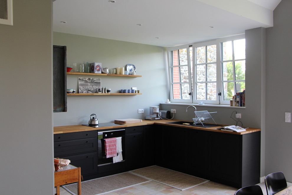 Inspiration for a mid-sized industrial l-shaped open plan kitchen in Rennes with an undermount sink, black cabinets, wood benchtops, panelled appliances, terra-cotta floors and no island.
