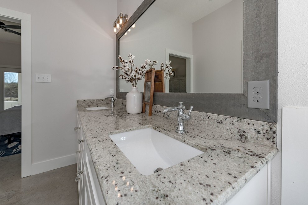 Photo of a mid-sized country master bathroom in Austin with shaker cabinets, white cabinets, a two-piece toilet, gray tile, white walls, concrete floors, an undermount sink, granite benchtops and grey floor.