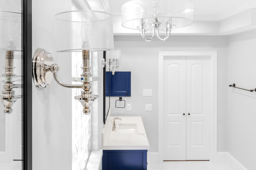 Photo of a mid-sized transitional master bathroom in Houston with furniture-like cabinets, blue cabinets, a freestanding tub, a curbless shower, a one-piece toilet, white tile, ceramic tile, grey walls, ceramic floors, an undermount sink, engineered quartz benchtops, white floor, a hinged shower door and white benchtops.