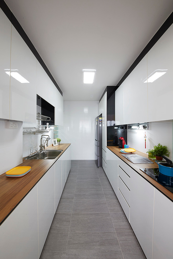This is an example of a mid-sized modern galley kitchen pantry in Singapore with flat-panel cabinets, white cabinets, wood benchtops, white splashback, slate floors and multiple islands.