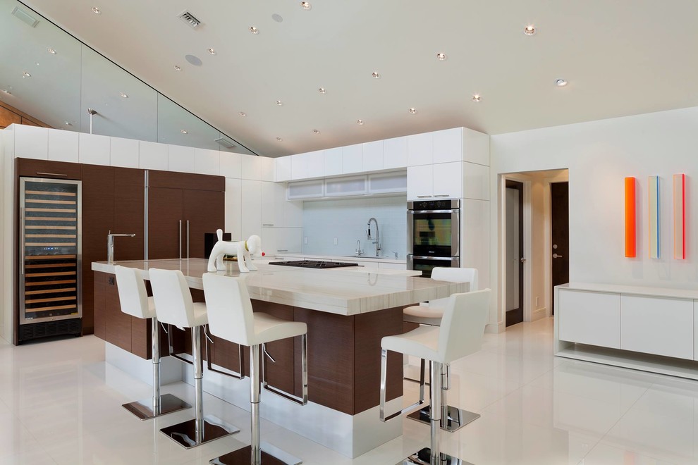 Large modern l-shaped eat-in kitchen in Miami with an undermount sink, flat-panel cabinets, white cabinets, marble benchtops, white splashback, ceramic splashback, panelled appliances, porcelain floors and with island.