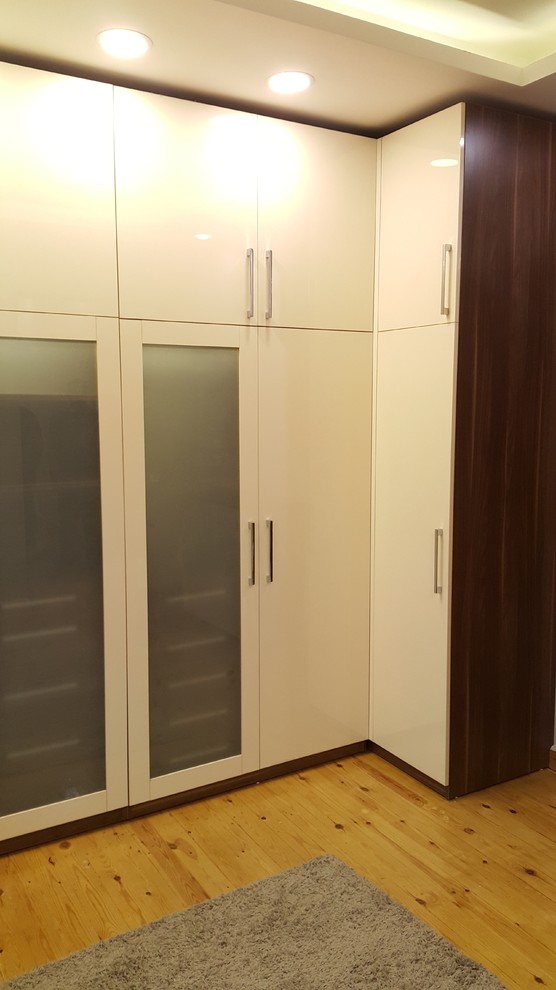 This is an example of a large modern gender-neutral dressing room in Other with glass-front cabinets, medium wood cabinets, laminate floors and yellow floor.