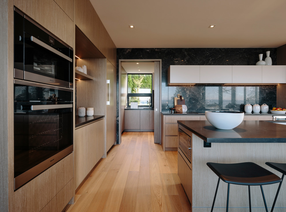 This is an example of a large contemporary galley eat-in kitchen in Vancouver with an undermount sink, flat-panel cabinets, medium wood cabinets, quartz benchtops, grey splashback, porcelain splashback, stainless steel appliances, medium hardwood floors, with island and grey benchtop.