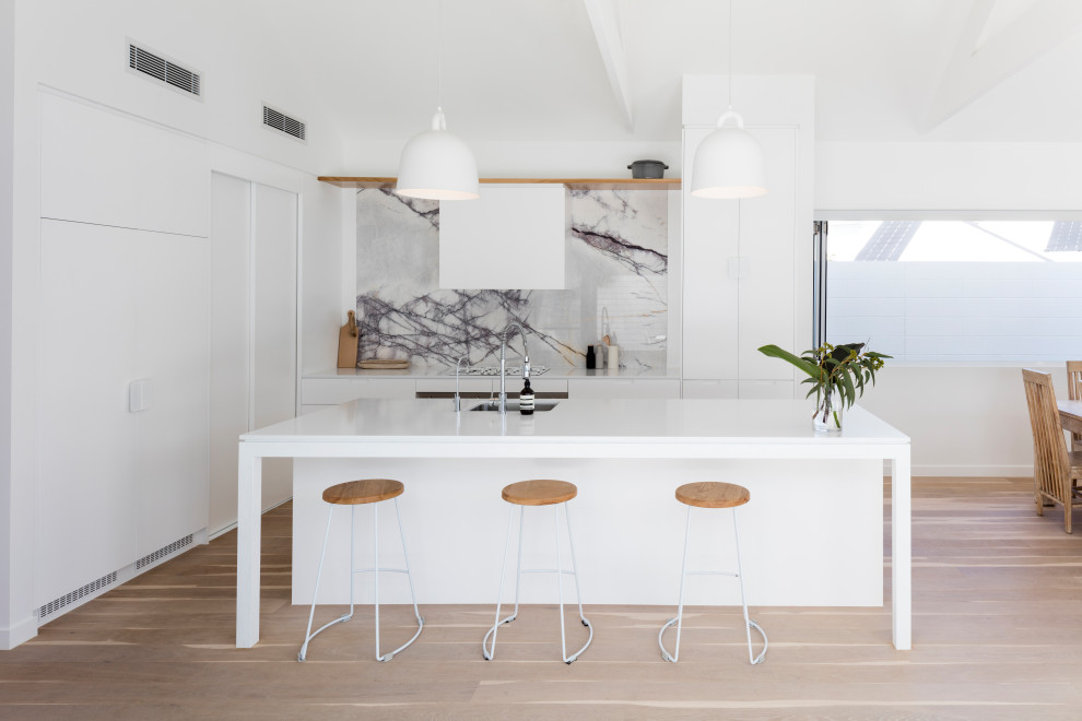 Inspiration for a large contemporary galley open plan kitchen in Sunshine Coast with an undermount sink, white cabinets, quartz benchtops, white splashback, marble splashback, panelled appliances, light hardwood floors, with island, white benchtop, flat-panel cabinets and beige floor.