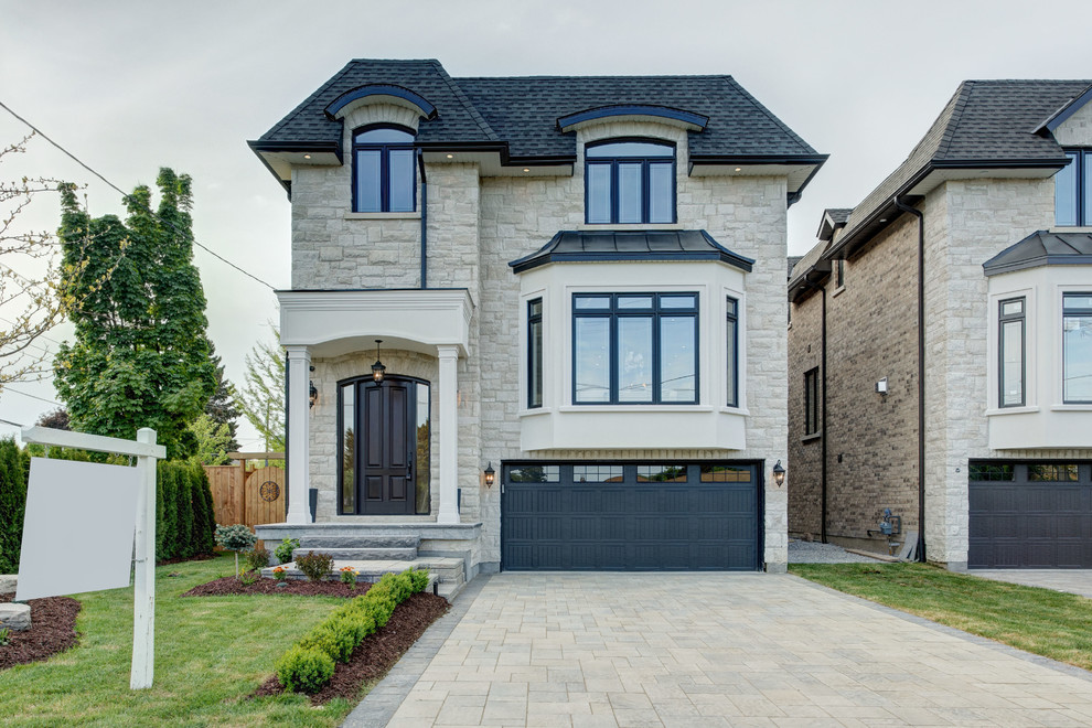 Photo of a mid-sized transitional two-storey beige house exterior in Toronto with stone veneer, a hip roof and a shingle roof.