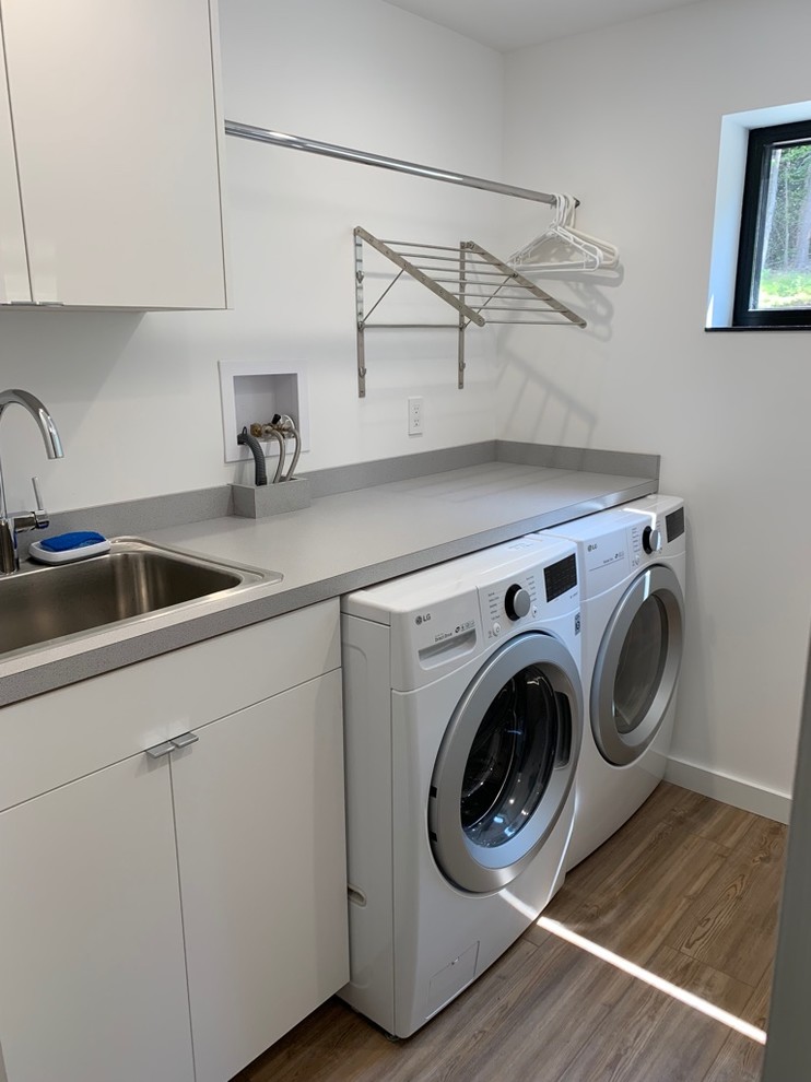 Design ideas for a mid-sized modern galley dedicated laundry room in Burlington with flat-panel cabinets, white cabinets, white walls, vinyl floors, a side-by-side washer and dryer and grey benchtop.