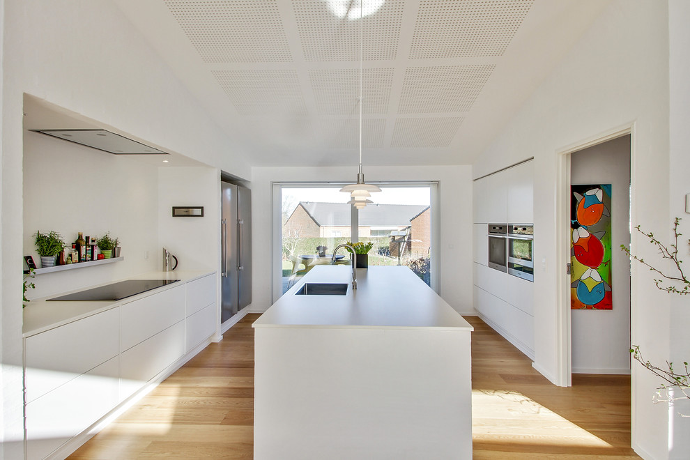 Mid-sized scandinavian galley eat-in kitchen in Aarhus with an integrated sink, flat-panel cabinets, white cabinets, laminate benchtops, stainless steel appliances, light hardwood floors and with island.