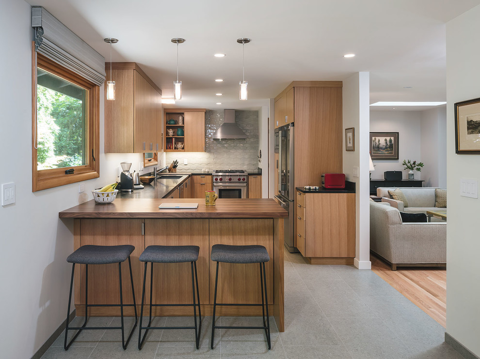 Midcentury u-shaped kitchen in Portland with an undermount sink, flat-panel cabinets, medium wood cabinets, soapstone benchtops, grey splashback, stainless steel appliances, a peninsula, grey floor and black benchtop.