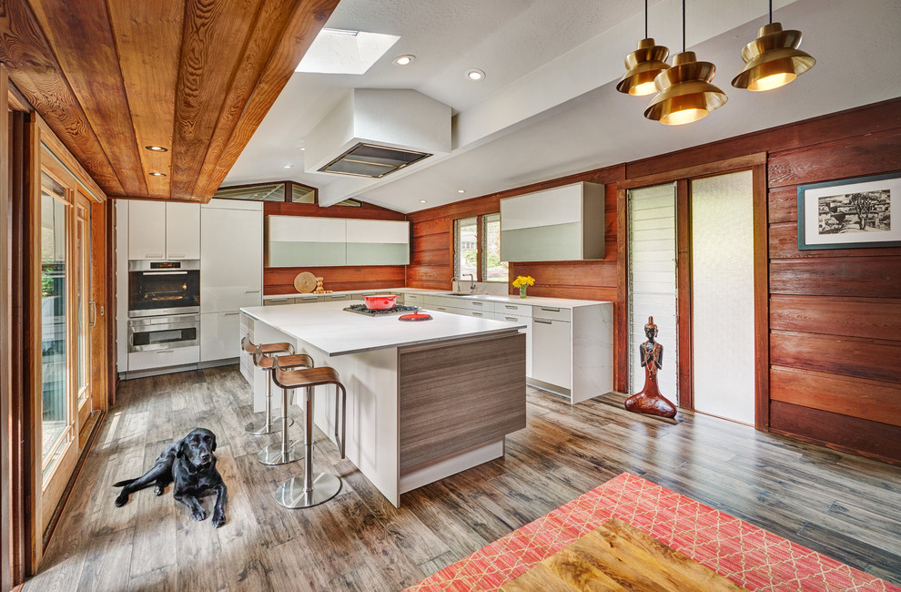 This is an example of a large midcentury l-shaped kitchen in Sacramento with an undermount sink, flat-panel cabinets, white cabinets, quartz benchtops, timber splashback, with island, brown floor, white benchtop and panelled appliances.