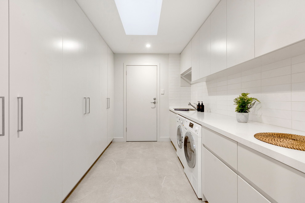 Inspiration for a mid-sized modern single-wall dedicated laundry room in Melbourne with an undermount sink, white cabinets, white walls, ceramic floors, a side-by-side washer and dryer, grey floor and white benchtop.