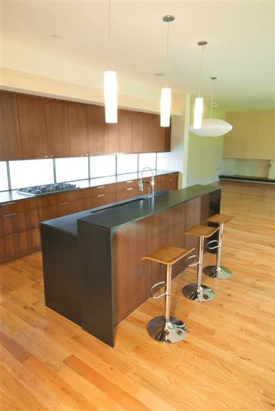Photo of a large modern l-shaped open plan kitchen in Dallas with an undermount sink, flat-panel cabinets, medium wood cabinets, stainless steel appliances, medium hardwood floors, with island and brown floor.