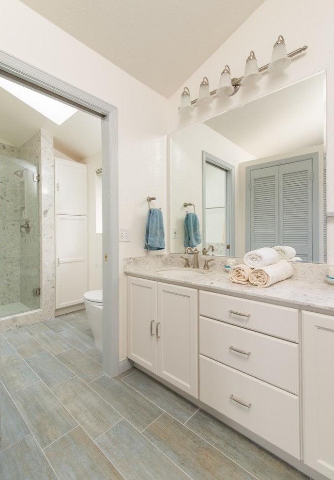 Inspiration for a large beach style master bathroom in San Diego with a drop-in sink, laminate benchtops, a drop-in tub, an alcove shower, a one-piece toilet, beige tile, ceramic tile, white walls, ceramic floors, recessed-panel cabinets and white cabinets.