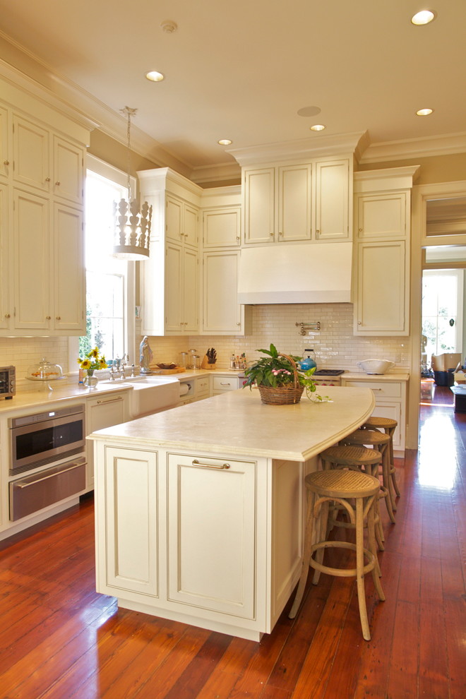 Photo of a traditional kitchen in New Orleans with a farmhouse sink, recessed-panel cabinets, beige cabinets, beige splashback, medium hardwood floors and with island.