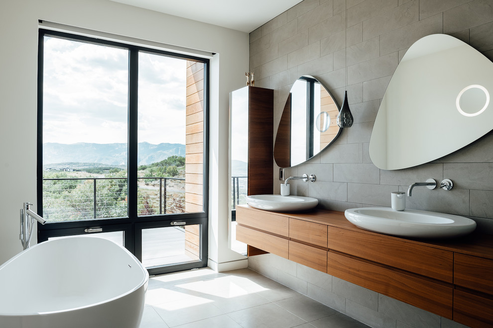 Inspiration for a modern master bathroom in Salt Lake City with flat-panel cabinets, medium wood cabinets, a freestanding tub, gray tile, white walls, a vessel sink, wood benchtops, grey floor and brown benchtops.