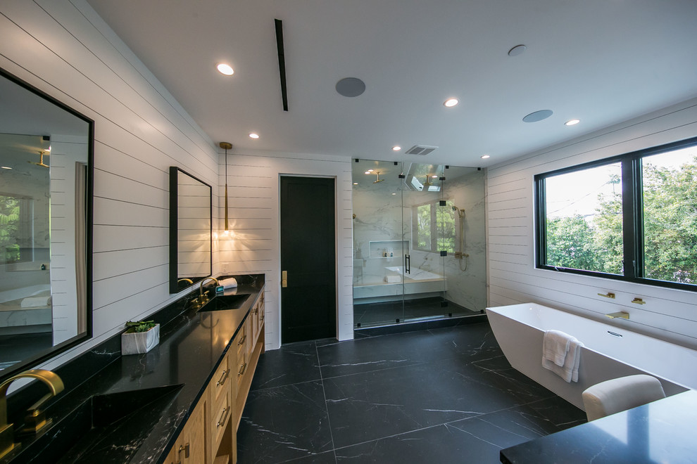 На фото: большая главная ванная комната в стиле модернизм с фасадами с выступающей филенкой, светлыми деревянными фасадами, отдельно стоящей ванной, угловым душем, белой плиткой, плиткой под дерево, белыми стенами, мраморным полом, монолитной раковиной, мраморной столешницей, черным полом, душем с распашными дверями, черной столешницей, сиденьем для душа, тумбой под две раковины, встроенной тумбой, многоуровневым потолком и деревянными стенами
