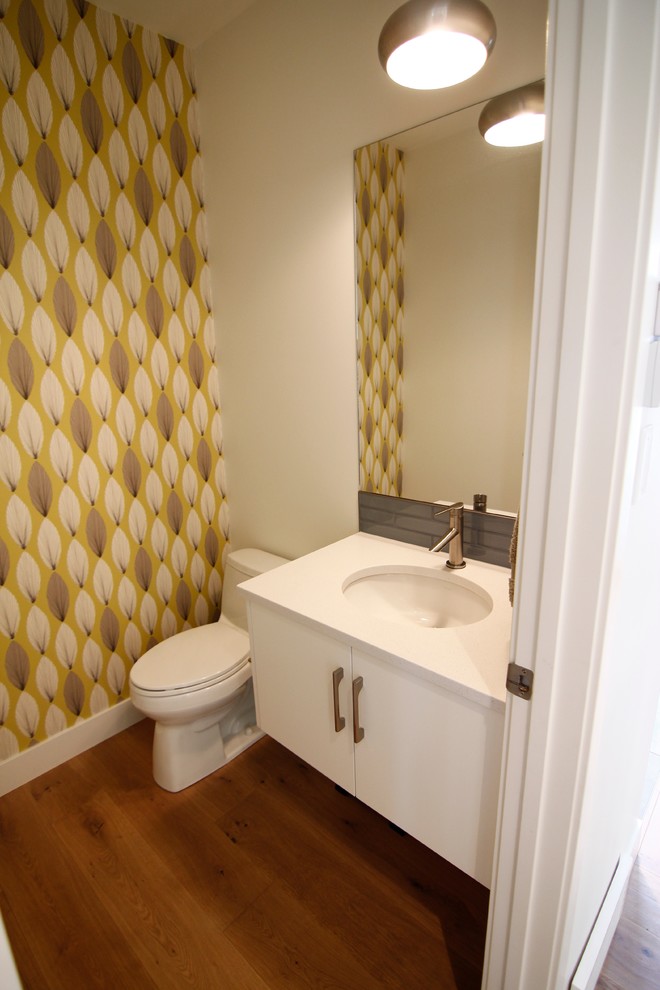 Inspiration for a small modern powder room in Calgary with a drop-in sink, flat-panel cabinets, white cabinets, a two-piece toilet, white tile, glass tile, yellow walls, medium hardwood floors and solid surface benchtops.