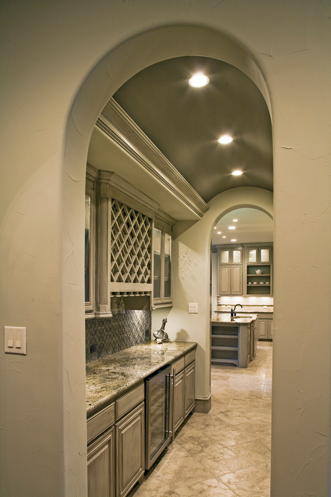 This is an example of an expansive mediterranean l-shaped kitchen in Dallas with an undermount sink, glass-front cabinets, grey cabinets, granite benchtops, metallic splashback, metal splashback, stainless steel appliances, travertine floors, with island, beige floor and multi-coloured benchtop.