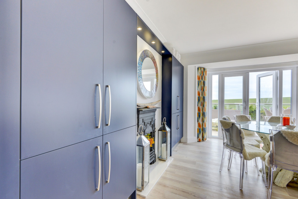 サセックスにあるお手頃価格の広いコンテンポラリースタイルのおしゃれなキッチン (一体型シンク、フラットパネル扉のキャビネット、青いキャビネット、珪岩カウンター、青いキッチンパネル、ガラス板のキッチンパネル、パネルと同色の調理設備、クッションフロア、茶色い床、白いキッチンカウンター) の写真