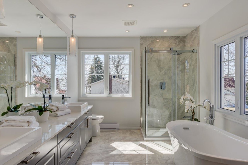 Inspiration for a mid-sized contemporary master bathroom in Montreal with raised-panel cabinets, grey cabinets, a freestanding tub, a corner shower, a two-piece toilet, white tile, marble, grey walls, porcelain floors, a vessel sink, engineered quartz benchtops, multi-coloured floor and a sliding shower screen.
