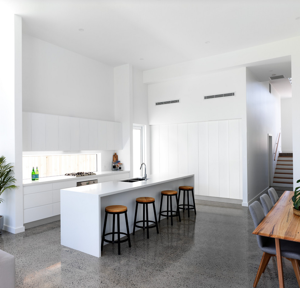 Design ideas for a beach style open plan kitchen in Sydney with a double-bowl sink, flat-panel cabinets, white cabinets, window splashback, concrete floors, with island, grey floor and white benchtop.