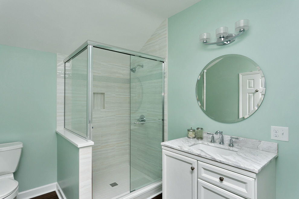 This is an example of a mid-sized transitional 3/4 bathroom in Raleigh with recessed-panel cabinets, white cabinets, an alcove tub, an alcove shower, a two-piece toilet, white tile, marble, blue walls, dark hardwood floors, an undermount sink, marble benchtops, brown floor and a sliding shower screen.