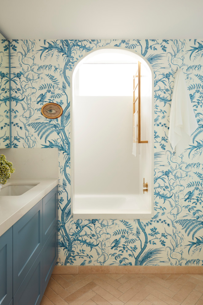 This is an example of a large eclectic bathroom in Sydney with blue cabinets, a shower/bathtub combo, an undermount sink, marble benchtops, beige benchtops, a single vanity, a built-in vanity and wallpaper.