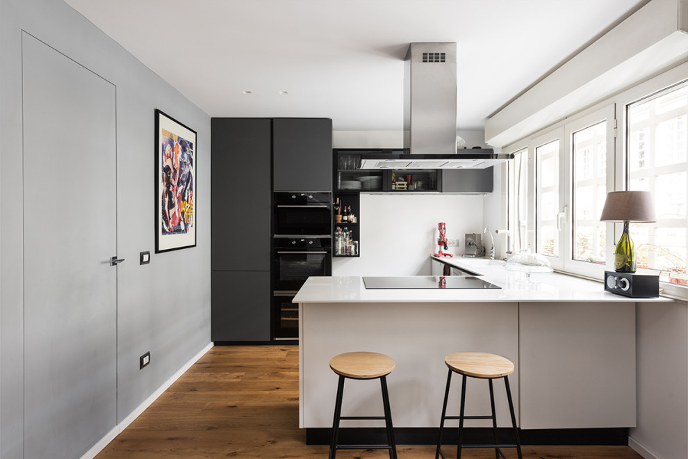 Design ideas for a small contemporary l-shaped open plan kitchen in Rome with an undermount sink, glass-front cabinets, white cabinets, quartz benchtops, white splashback, black appliances, light hardwood floors, with island, yellow floor, white benchtop and recessed.