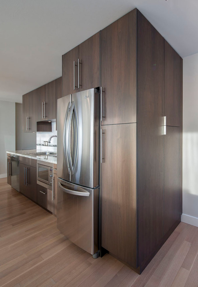 This is an example of a mid-sized contemporary single-wall open plan kitchen in Vancouver with flat-panel cabinets, medium wood cabinets, granite benchtops, stainless steel appliances, a double-bowl sink, white splashback, subway tile splashback, light hardwood floors, with island and beige floor.