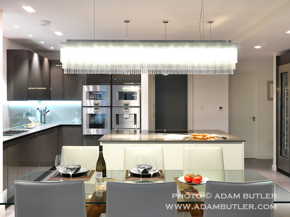 Inspiration for a mid-sized contemporary l-shaped eat-in kitchen in London with an integrated sink, flat-panel cabinets, grey cabinets, granite benchtops, grey splashback, glass sheet splashback, stainless steel appliances, ceramic floors and with island.