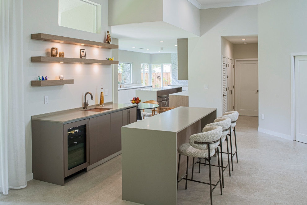 This is an example of a large modern u-shaped home bar in Miami with an undermount sink, flat-panel cabinets, light wood cabinets, quartz benchtops, grey splashback, marble splashback, porcelain floors, beige floor and white benchtop.