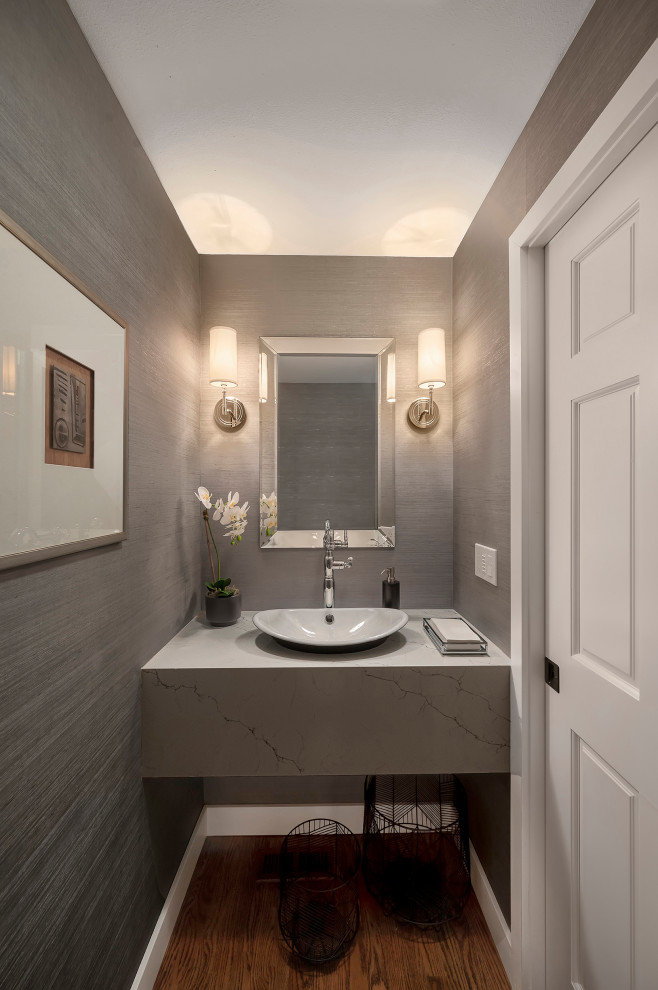 Small transitional powder room in Seattle with open cabinets, a one-piece toilet, grey walls, medium hardwood floors, a vessel sink, engineered quartz benchtops, brown floor, white benchtops, a floating vanity and wallpaper.