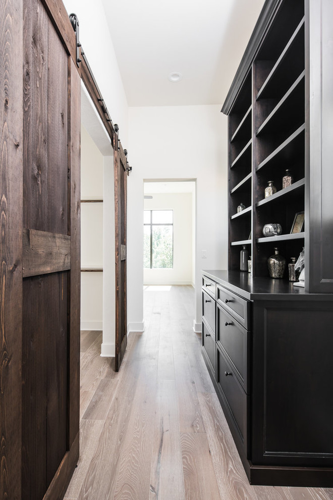 Photo of a mid-sized contemporary gender-neutral walk-in wardrobe in Austin with shaker cabinets, dark wood cabinets, light hardwood floors and beige floor.