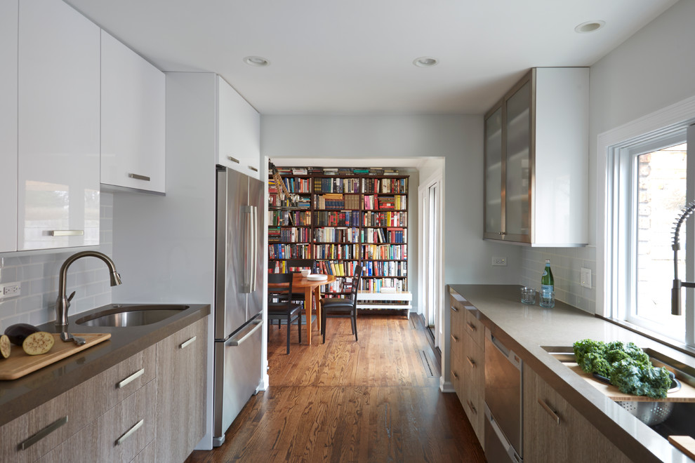 Inspiration for a timeless medium tone wood floor and brown floor enclosed kitchen remodel with a double-bowl sink, flat-panel cabinets, distressed cabinets, solid surface countertops, white backsplash, glass tile backsplash, stainless steel appliances and no island