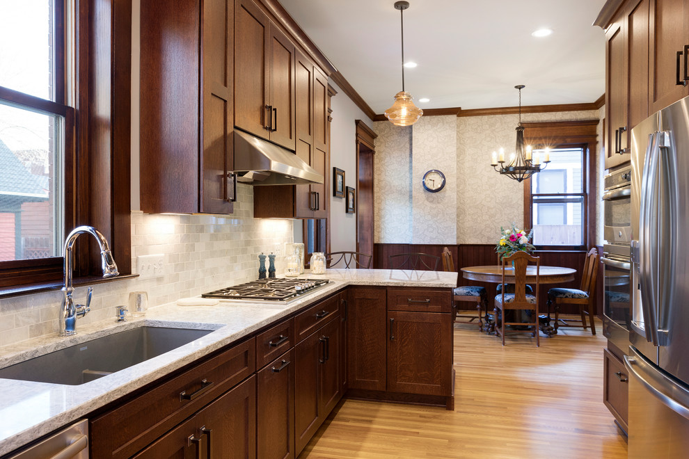 This is an example of a large arts and crafts u-shaped eat-in kitchen in Minneapolis with an undermount sink, medium wood cabinets, quartz benchtops, marble splashback, stainless steel appliances, light hardwood floors, a peninsula, yellow floor, shaker cabinets and white splashback.