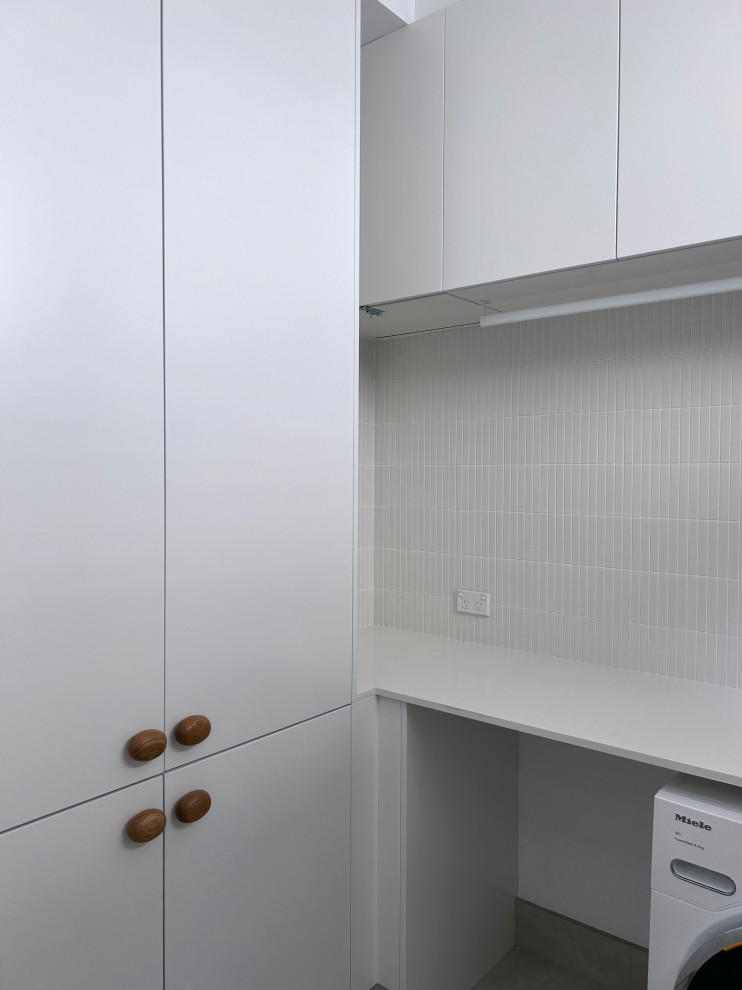 Photo of a small modern l-shaped dedicated laundry room in Sydney with a single-bowl sink, flat-panel cabinets, white cabinets, quartz benchtops, green splashback, ceramic splashback, white walls, ceramic floors, a side-by-side washer and dryer, grey floor and white benchtop.