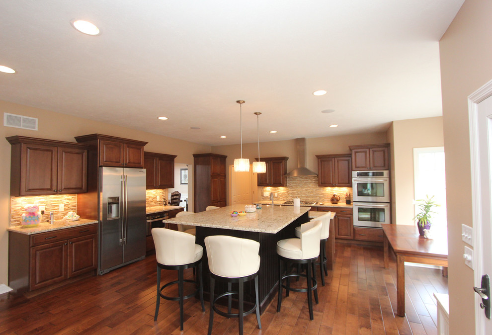 Inspiration for a large transitional l-shaped medium tone wood floor eat-in kitchen remodel with a farmhouse sink, raised-panel cabinets, medium tone wood cabinets, granite countertops, beige backsplash, glass tile backsplash, stainless steel appliances, beige walls and an island