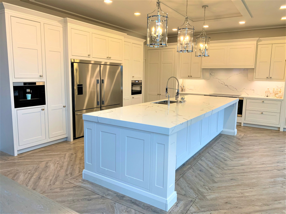 Large traditional l-shaped kitchen/diner in Other with a double-bowl sink, shaker cabinets, light wood cabinets, quartz worktops, white splashback, black appliances, vinyl flooring, an island and white worktops.