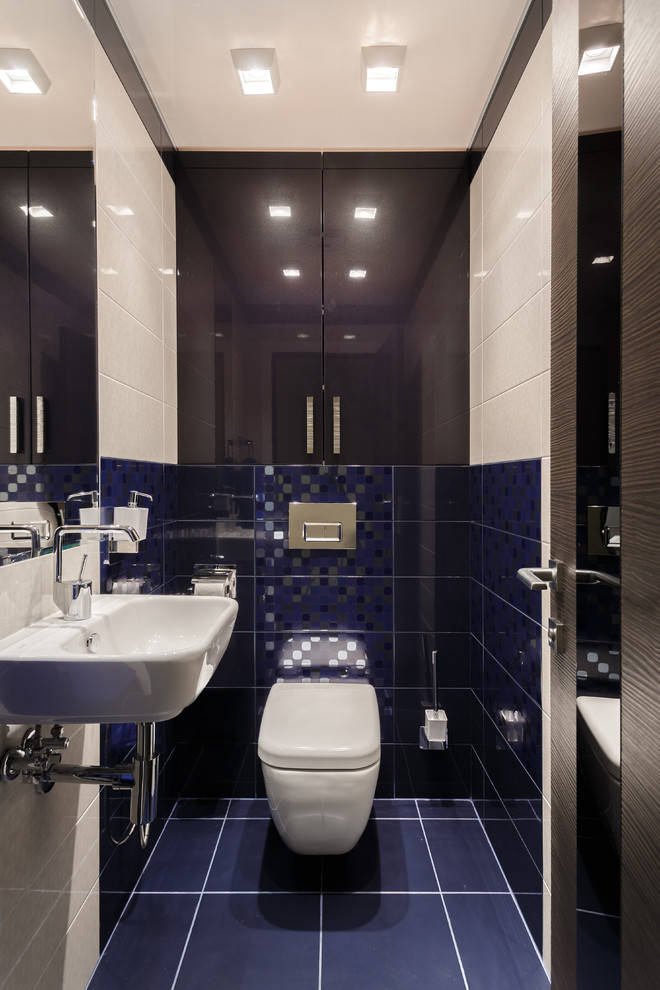 Photo of a small contemporary powder room in Other with flat-panel cabinets, blue cabinets, a wall-mount toilet, blue tile, ceramic tile, beige walls, ceramic floors, a wall-mount sink and blue floor.