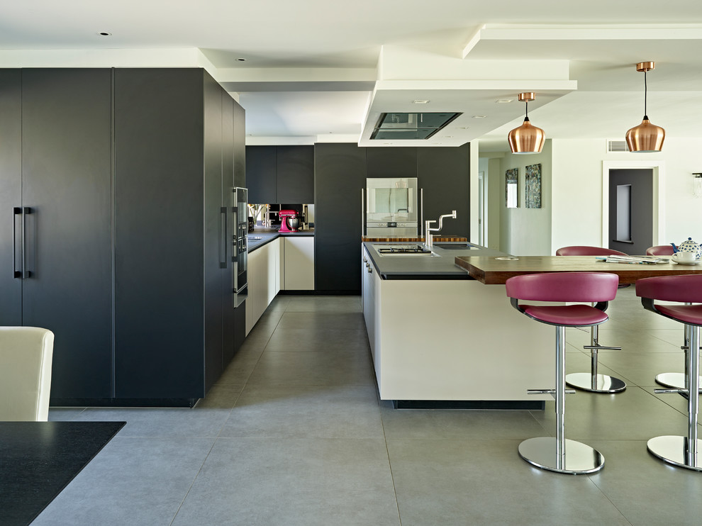 This is an example of a large contemporary l-shaped open plan kitchen in Hertfordshire with flat-panel cabinets, concrete floors, with island, grey floor and black benchtop.