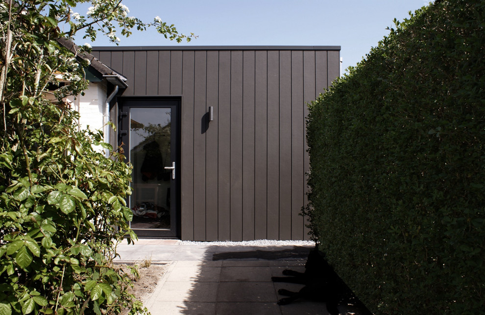 Photo of a small contemporary one-storey black exterior with wood siding, a flat roof, a mixed roof, a black roof and board and batten siding.